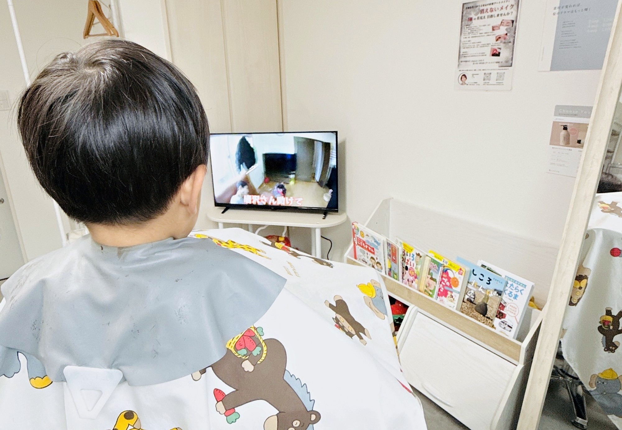 動物柄のケープを着たお子さんの後ろ姿。前にテレビと絵本の棚